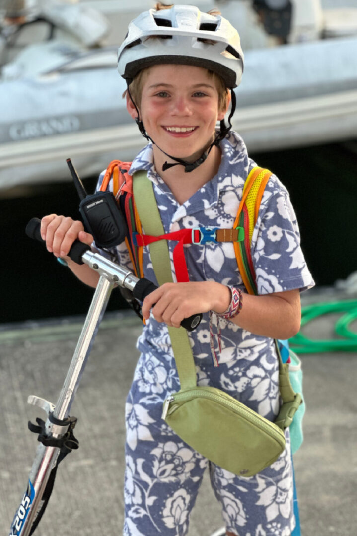 A young boy holding a backpack and a cell phone.