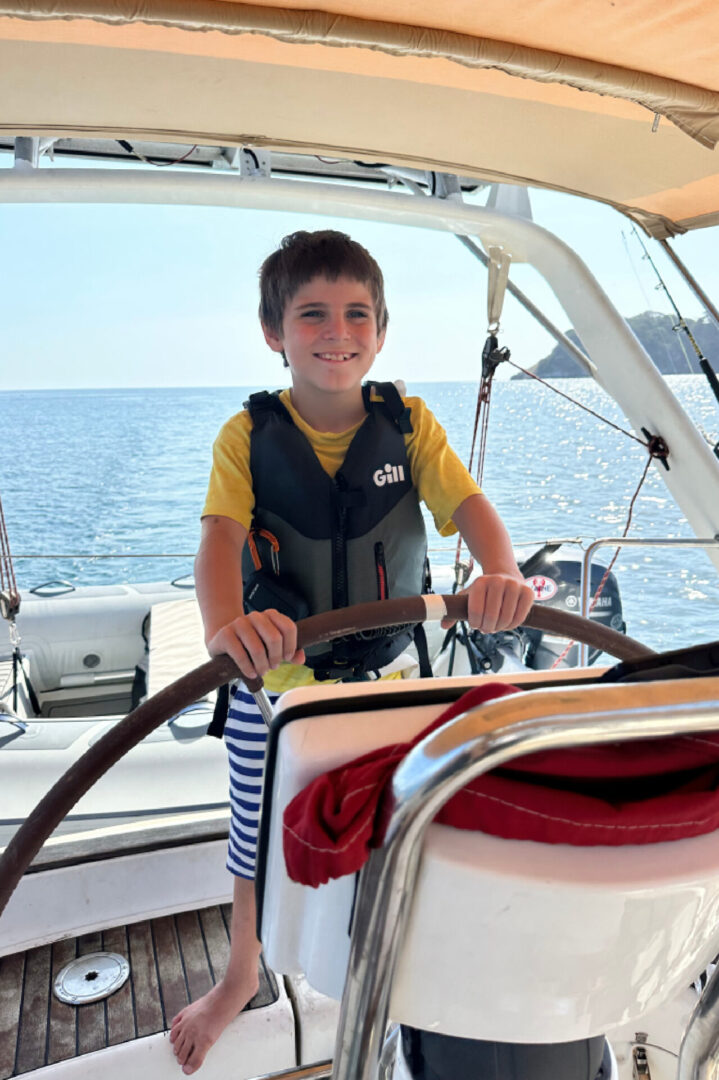 A young boy is sitting at the steering wheel of a boat.