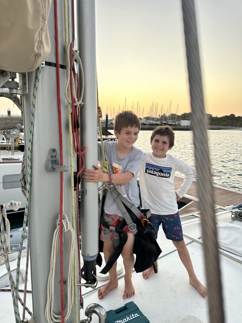 Two boys standing on a boat in the water.